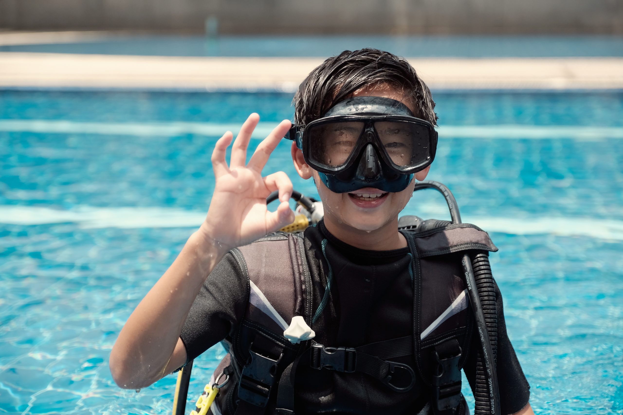 Young little Asian boy scuba diver showing ok hand signal, diving lessons for beginners